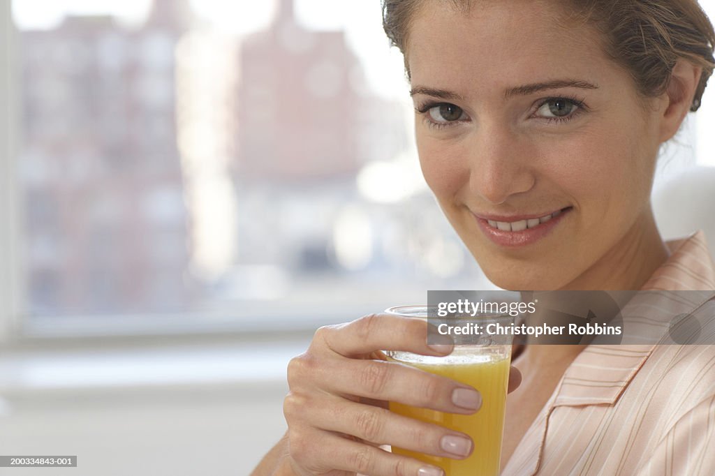 Young woman wearing pyjamas holding glass of juice, smiling, portrait