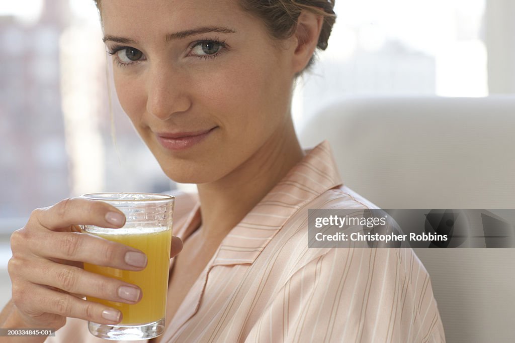 Young woman wearing pyjamas holding glass of juice, close-up, portrait