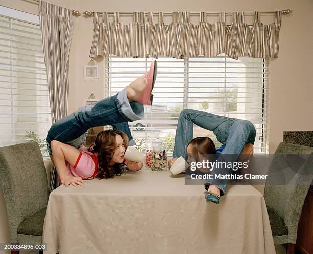 young female contortionists sipping from mugs on table, side view - slangenmens stockfoto's en -beelden