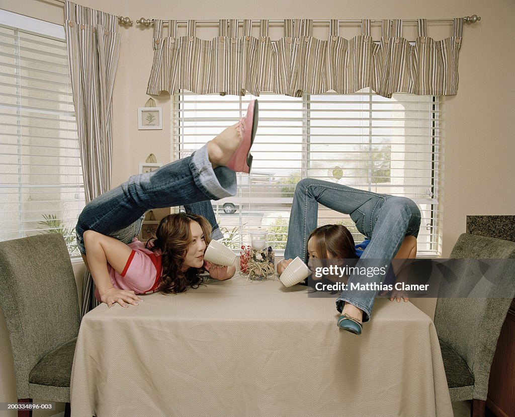 Young female contortionists sipping from mugs on table, side view