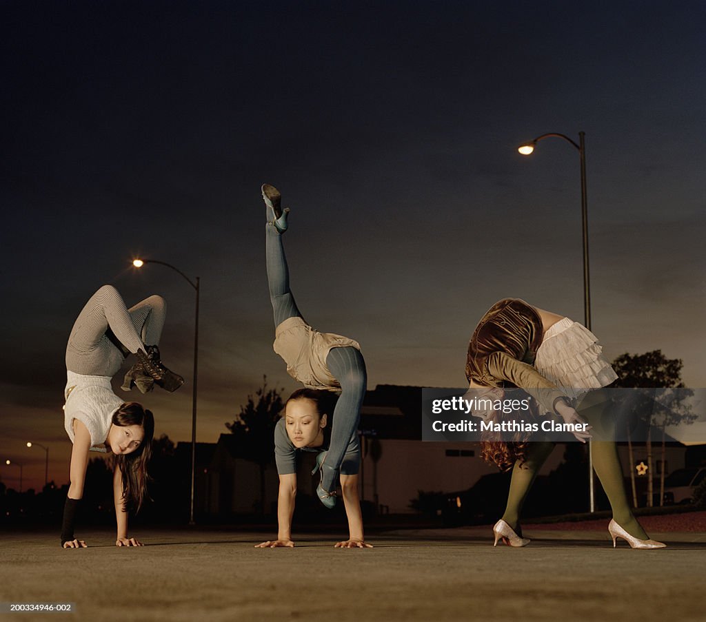 Three young female contortionists practicing on road, dusk