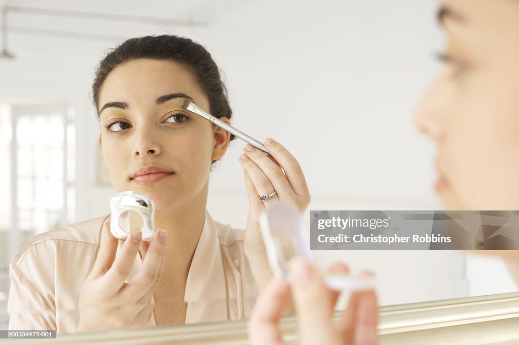 Young woman applying make-up in mirror, using brush, close-up