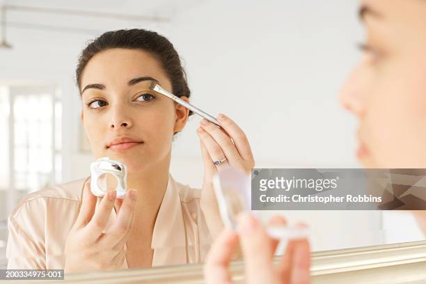 young woman applying make-up in mirror, using brush, close-up - trucco per il viso foto e immagini stock