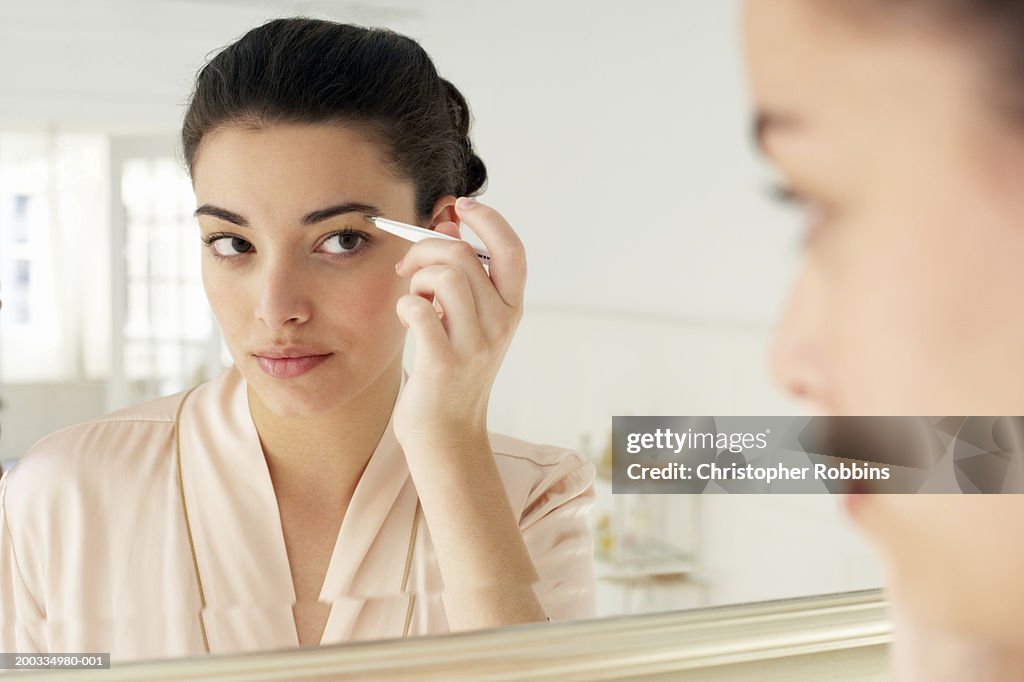 Young woman plucking eyebrows, close-up, reflection in mirror