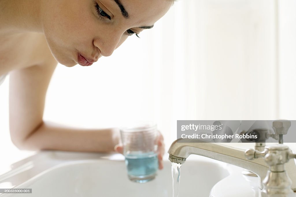 Young woman rinsing mouth, leaning over sink, close-up