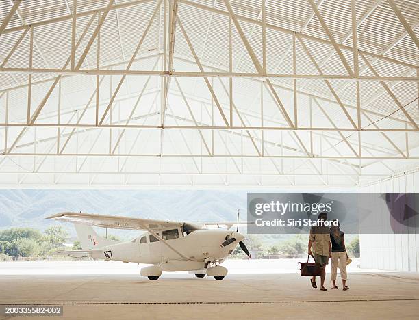 young couple in hangar, private plane in background - aviacion fotografías e imágenes de stock