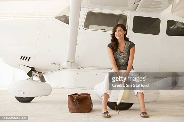 young woman sitting on wheel of private plane - driekwart broek stockfoto's en -beelden
