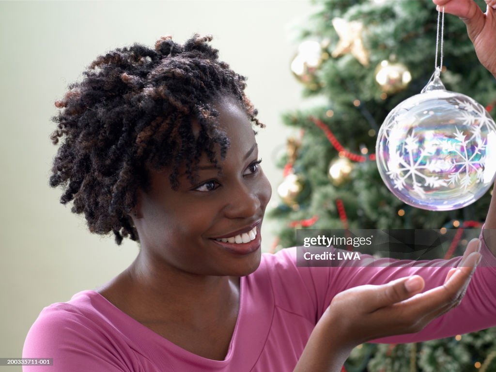 Young woman looking at Christmas ornament, tree in background, smiling