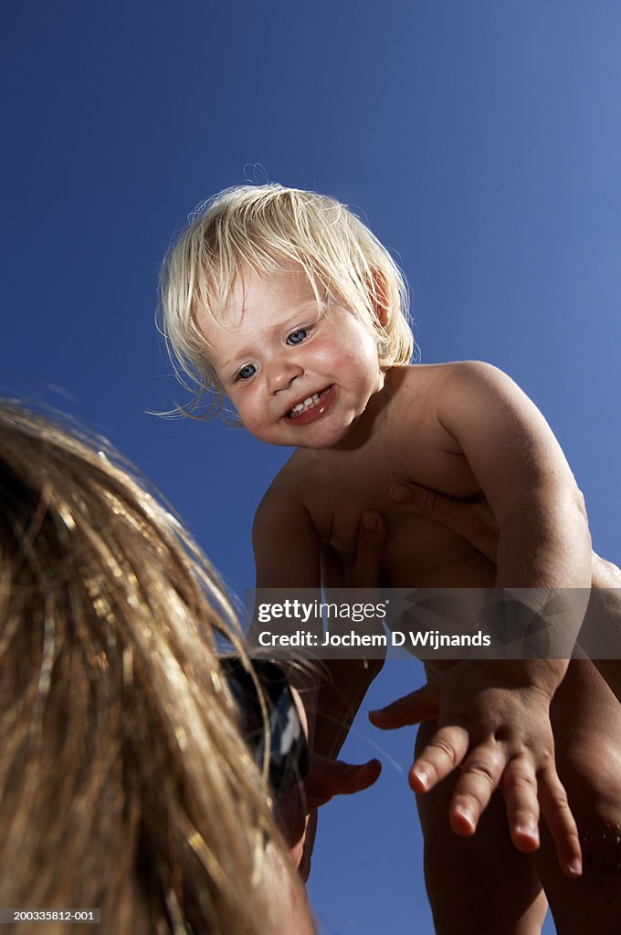 Mother holding up baby girl (18-21 months), close up, low angle