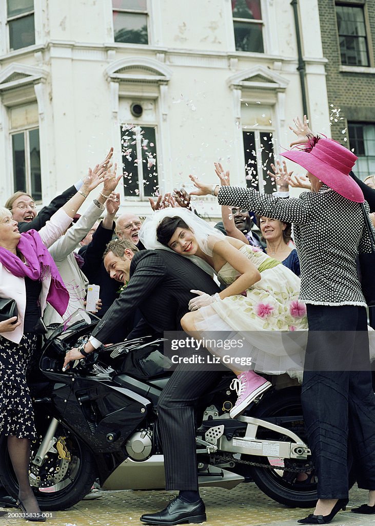 Wedding guests throwing confetti over bride and groom on motorbike