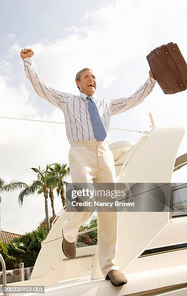 mature businessman stepping off yacht, arms raised, smiling - holding above head stock pictures, royalty-free photos & images