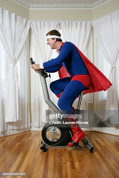 man in superhero costume on exercise bike, side view - laufen sport stock pictures, royalty-free photos & images