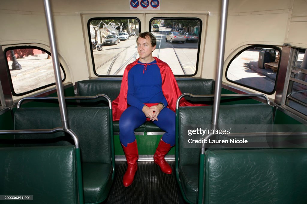 Man in superhero costume riding bus, hands clasped