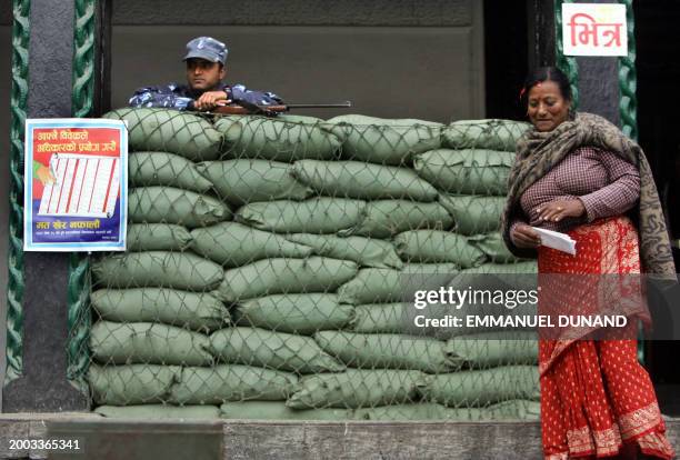 Nepalese voter walks out, ballot in hand, of a polling booth set up behind army sand bags under the close watch of an armed Nepalese policeman during...