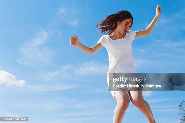 young woman jumping outdoors, low angle view - short sleeved stockfoto's en -beelden