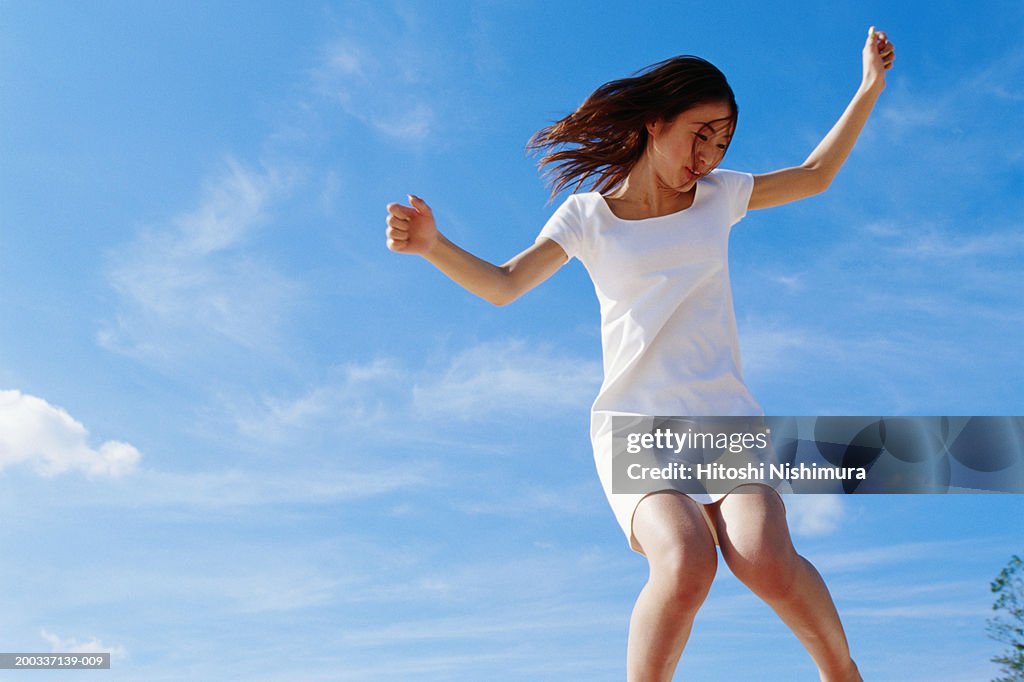 Young woman jumping outdoors, low angle view