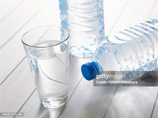 glass of water with plastic water bottles on wood - destilliertes wasser stock-fotos und bilder