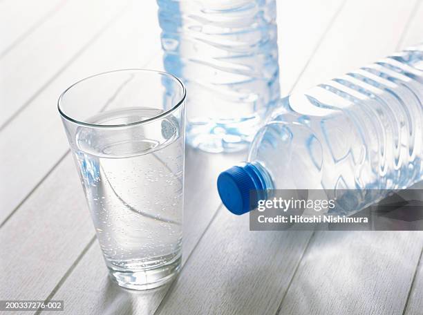 glass of water with plastic water bottles on wood - purified water stock-fotos und bilder