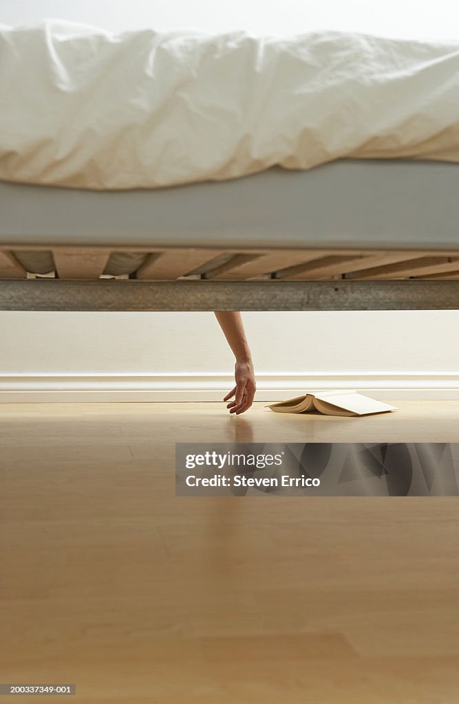 Woman's hand hanging over bed, view from below bed, book on floor