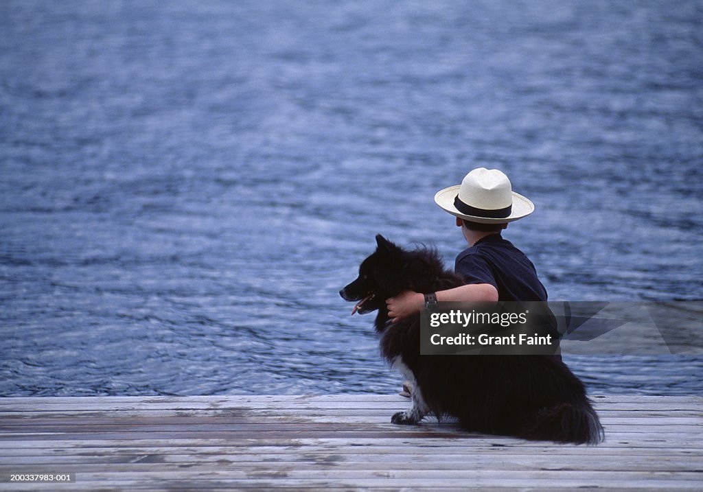 Boy (10-12) sitting on dock with dog, rear view