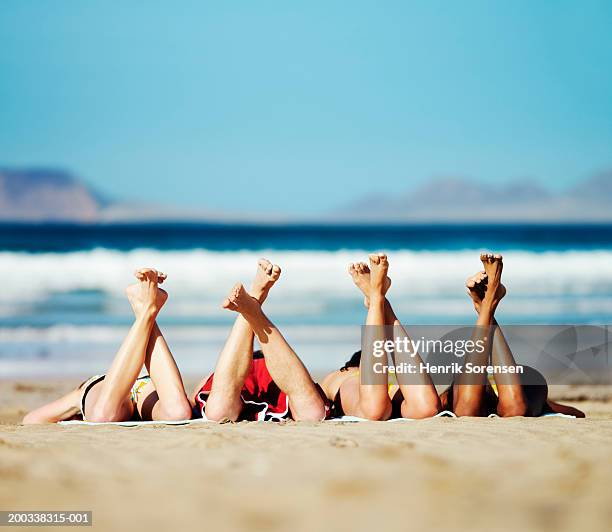 three young women and young man lying on beach, feet in air - woman lying on stomach with feet up fotografías e imágenes de stock