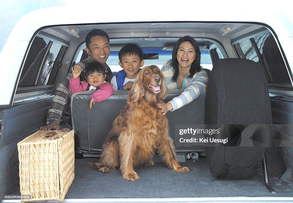 Family of four and dog in back of car, portrait, view through boot