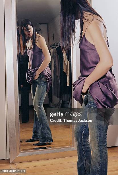 young woman trying on dress, undoing jeans in front of mirror - woman mirror dress stock-fotos und bilder