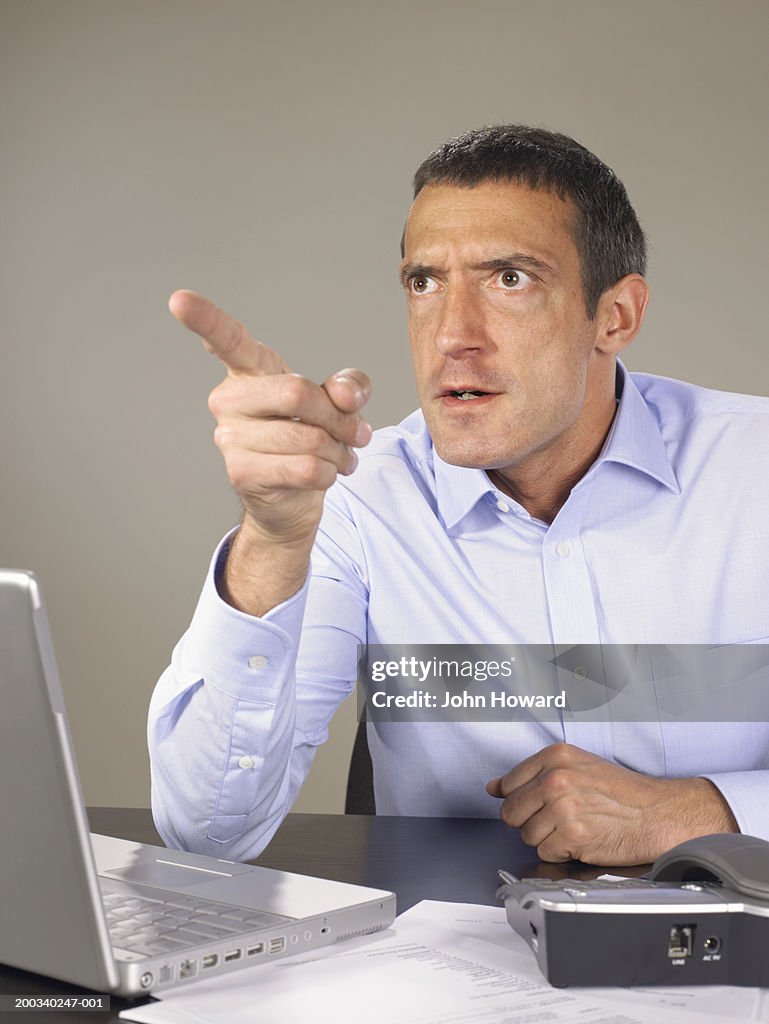 Man sitting at laptop, resting elbow on desk, pointing