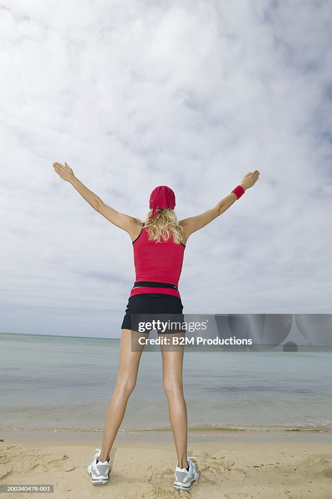 Young woman standing on beach, arms outstretched, rear view