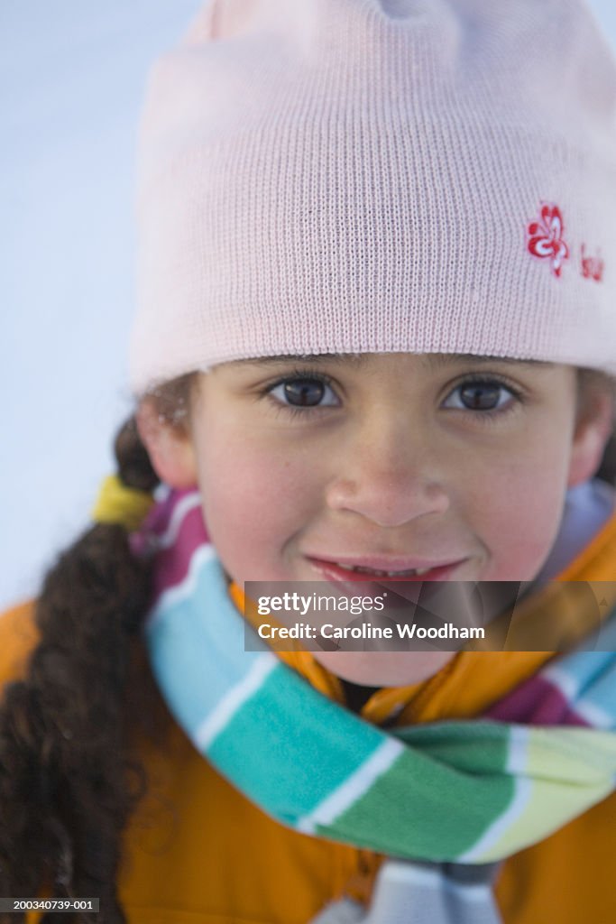 Girl (5-7) wearing knit hat and scarf, smiling, portrait