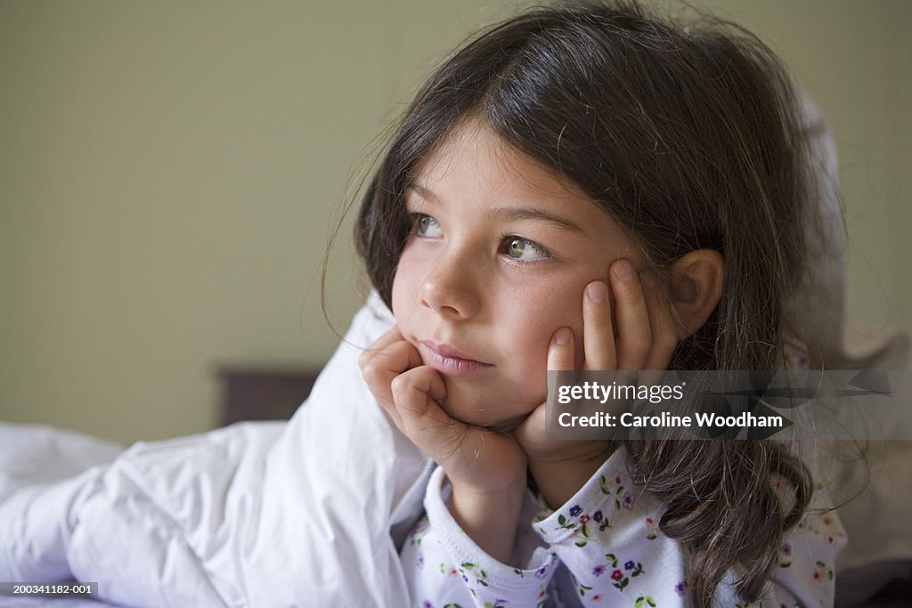 Girl (4-6) lying on bed, resting chin on hands, looking away