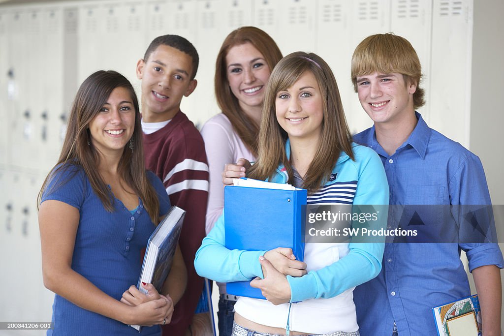 Five teenagers (14-16) standing beside lockers, smiling, portrait