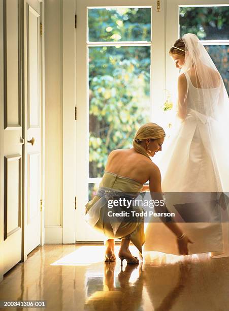 bridesmaid adjusting bride's dress beside french doors, rear view - familys revenge of the bridesmaids stockfoto's en -beelden