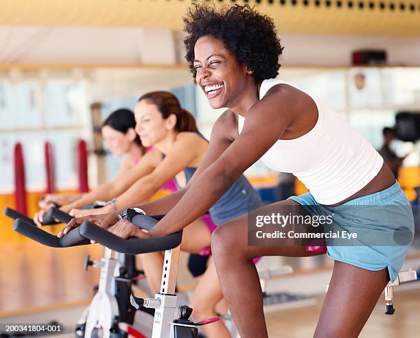 women sitting on exercising bikes in gym, side view - exercise bike fotografías e imágenes de stock