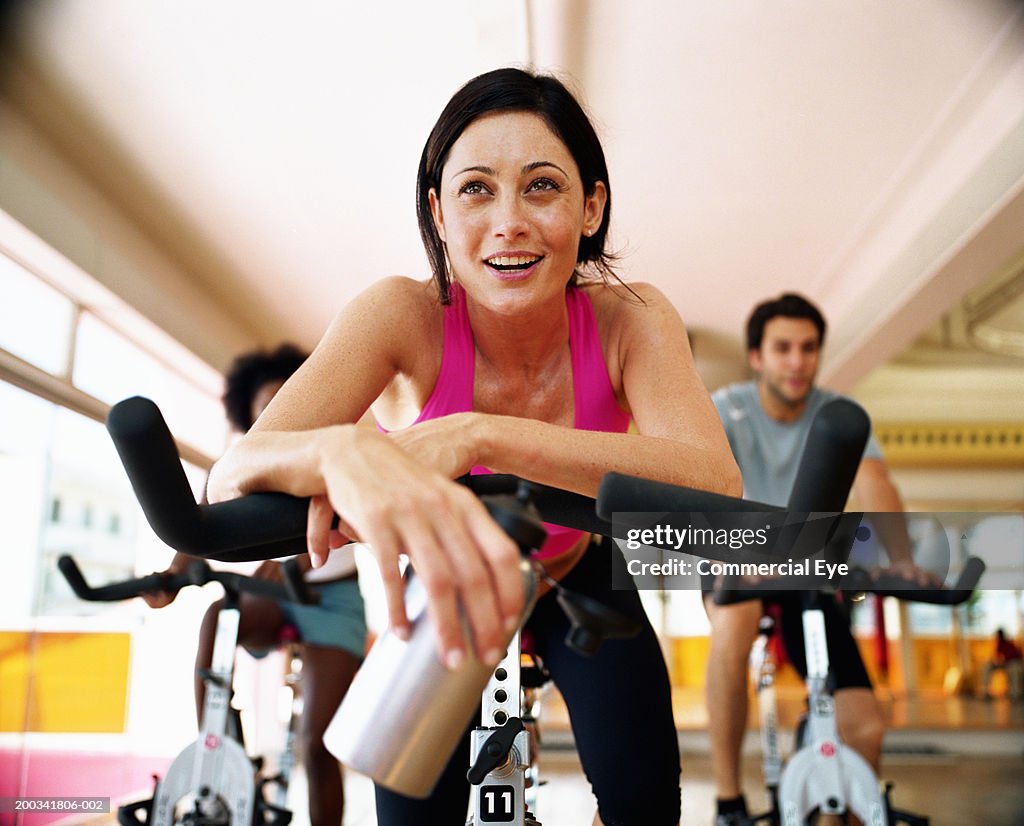 Three people sitting on exercising bikes in gym, close-up