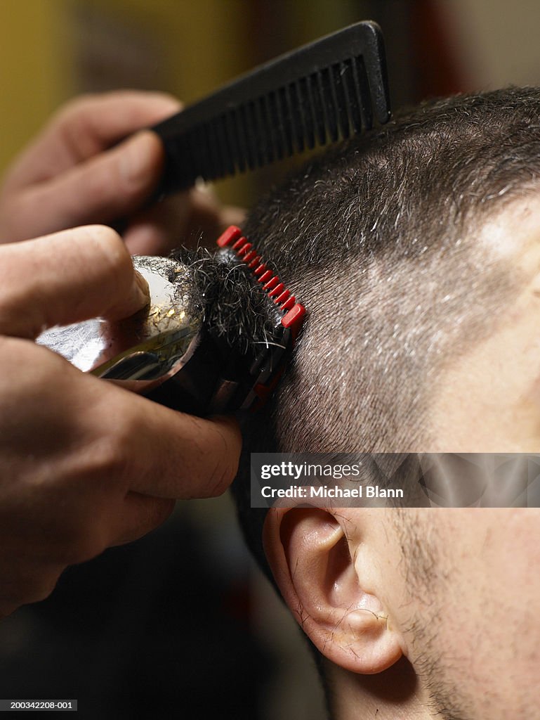 Barber cutting man's hair with electric razor, close-up of hands