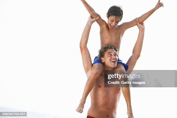 son (8-10) sitting on father's shoulders on beach, smiling - barefoot men - fotografias e filmes do acervo