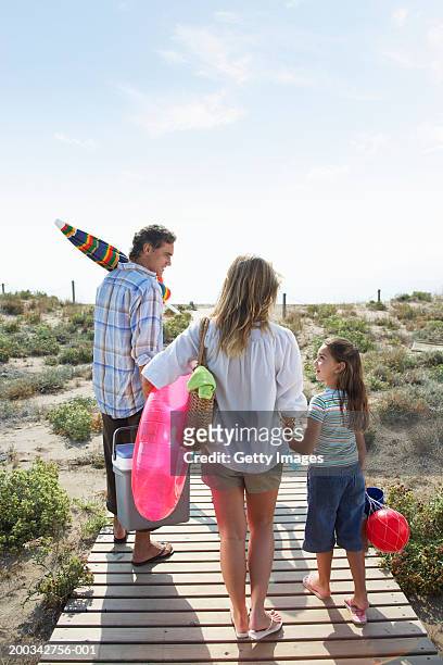 parents and daughter (6-8) on beach path carrying picnic box and toys - barcelona coast stock pictures, royalty-free photos & images