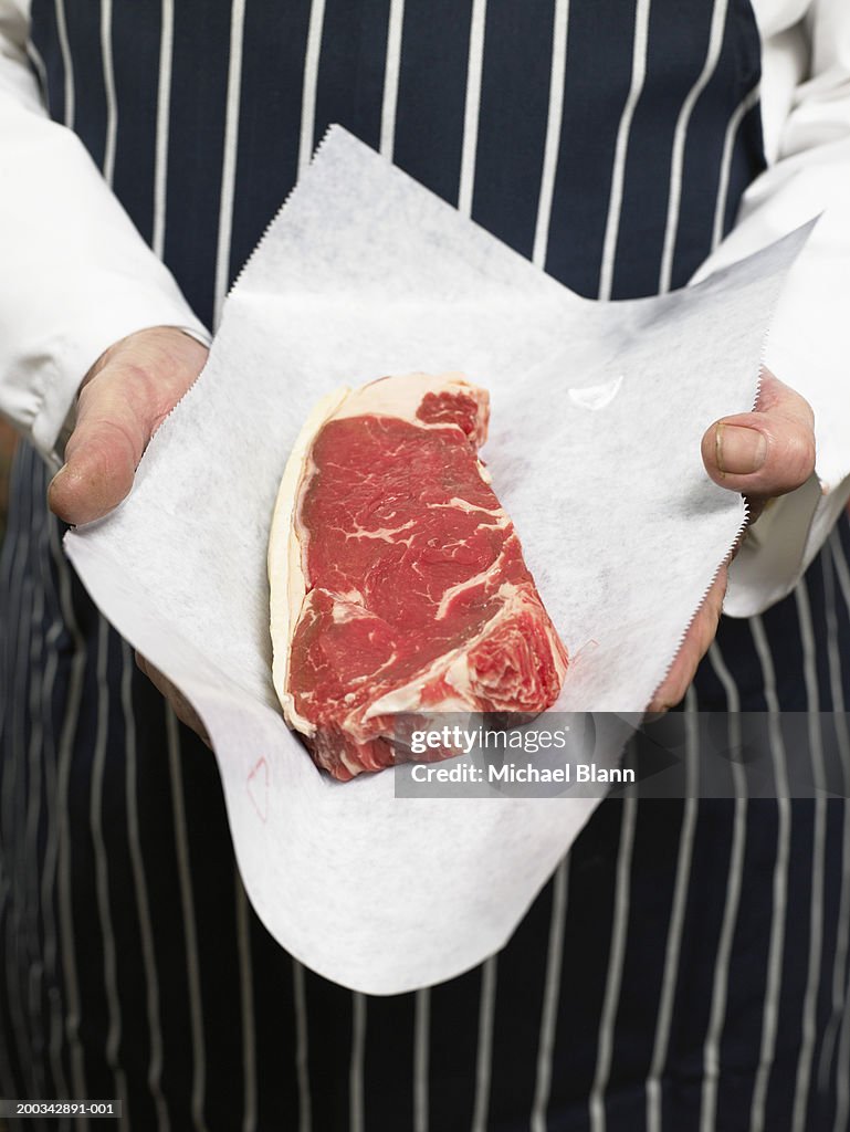Senior male butcher holding sirloin of steak, mid section