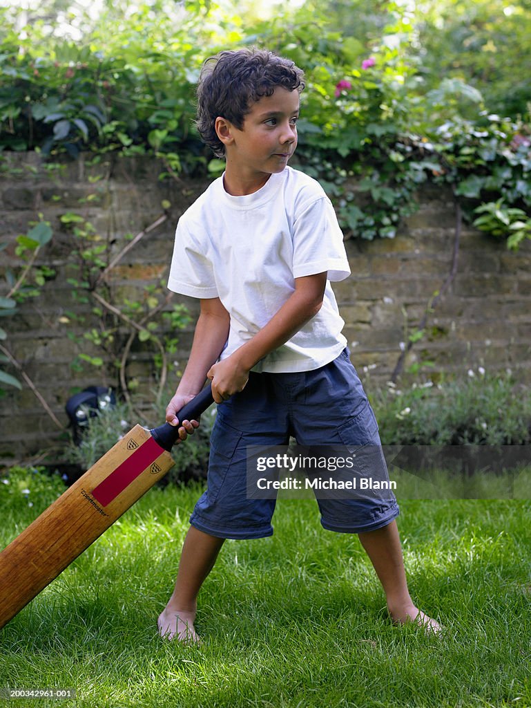 Boy (6-8) playing cricket in garden, holding bat