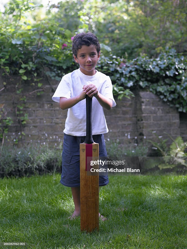 Boy (6-8) playing cricket in garden, leaning on bat, portrait