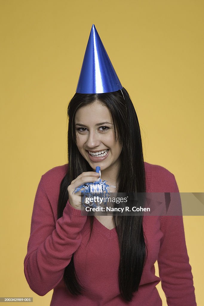 Young woman wearing party hat, holding party horn blower, portrait