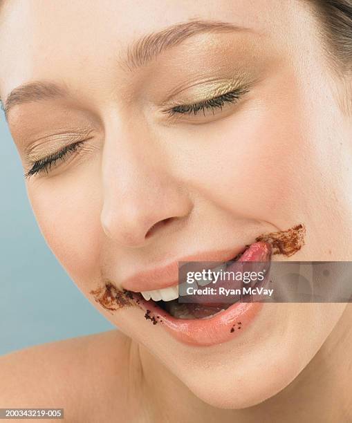 young woman licking chocolate frosting off face, eyes closed, close-up - chocolate face stock pictures, royalty-free photos & images