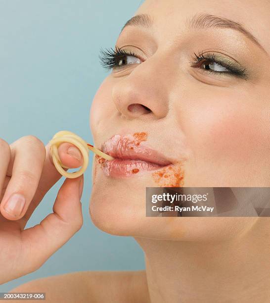 young woman eating strand of spaghetti, pasta sauce on face, close-up - human mouth stock pictures, royalty-free photos & images