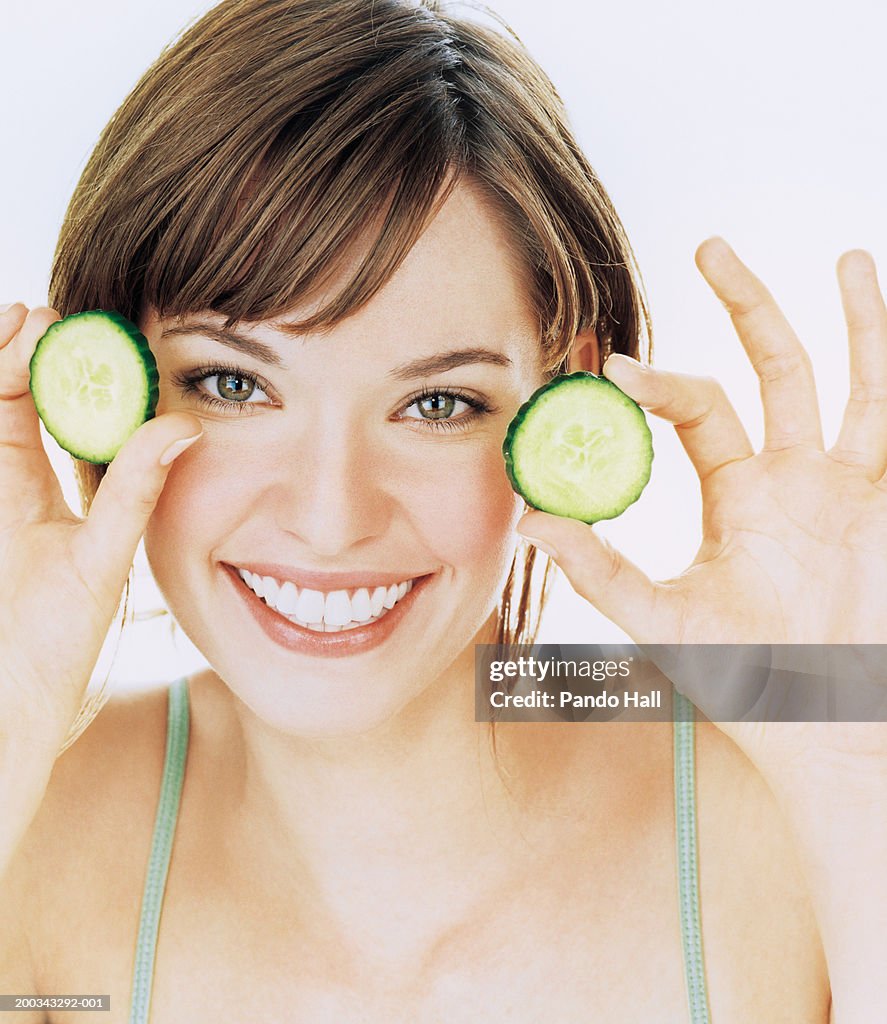 Young woman holding up slices of cucumber, smiling, portrait, close-up