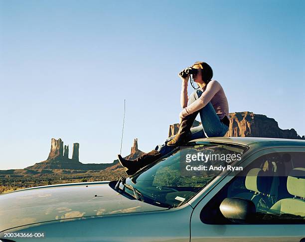 woman sitting on roof of car, using binoculars, side view - sitting on top of car stock pictures, royalty-free photos & images