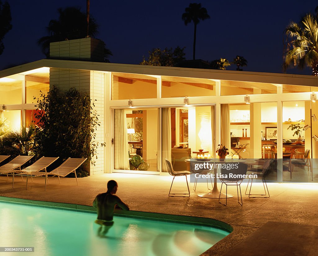 Man standing in pool, house lit at night