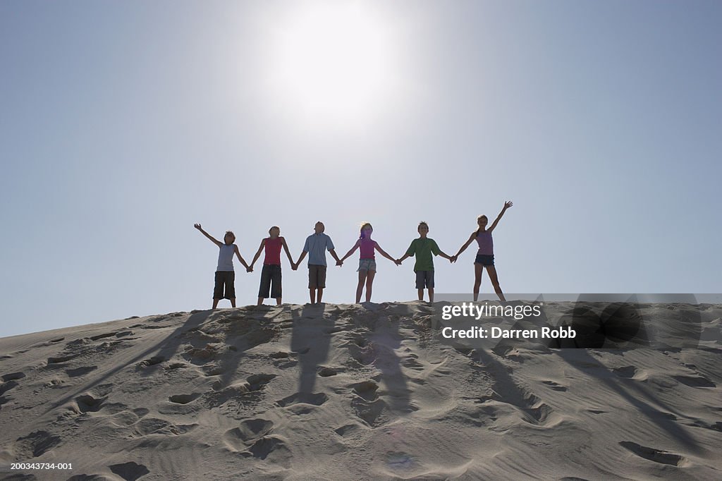 Group of children (9-11) standing on sand dune, holding hands in row