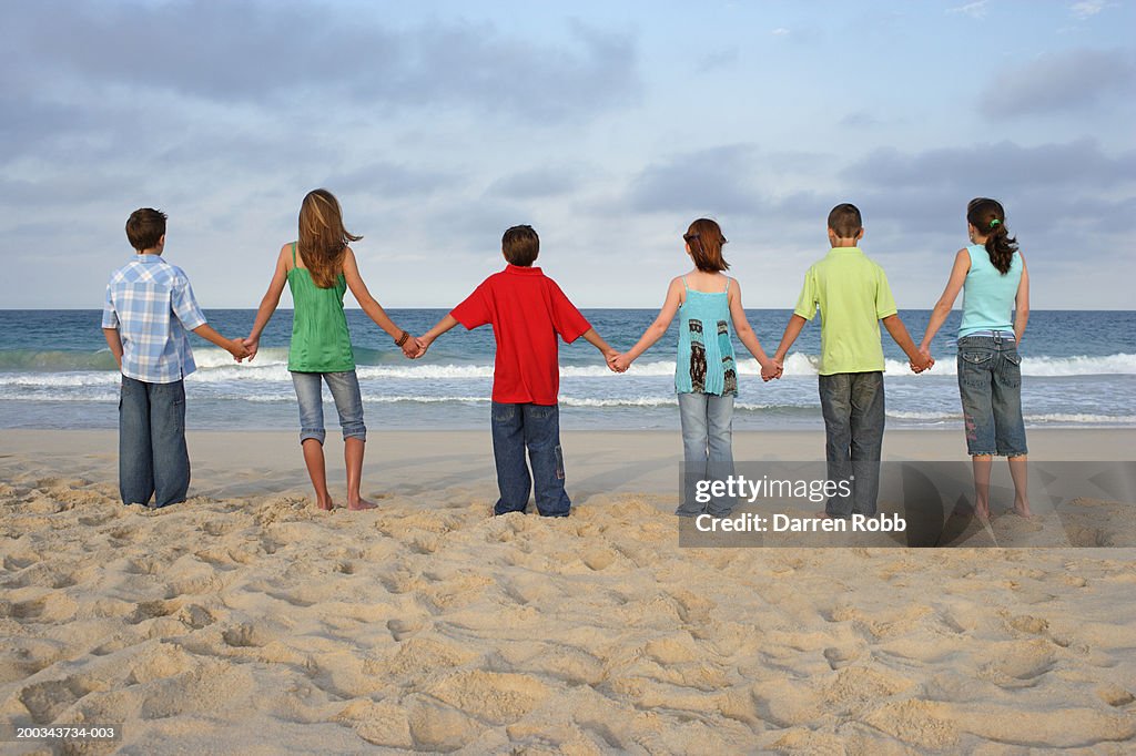 Group of children (9-11) holding hands in row on beach, rear view