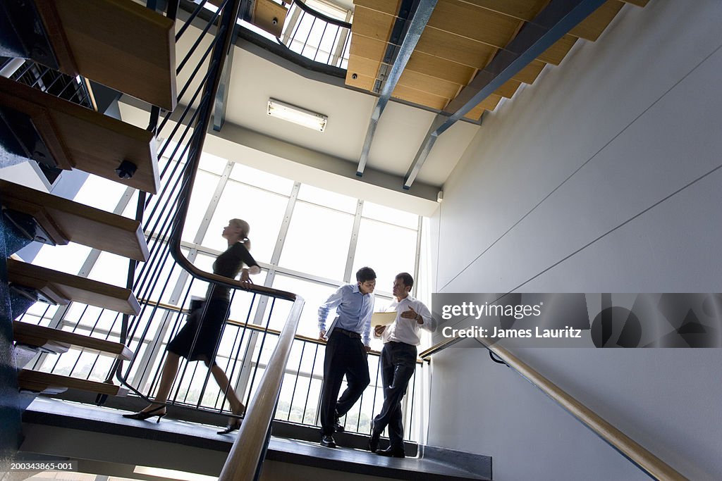 Two businessmen talking in stairwell, woman passing, low angle view